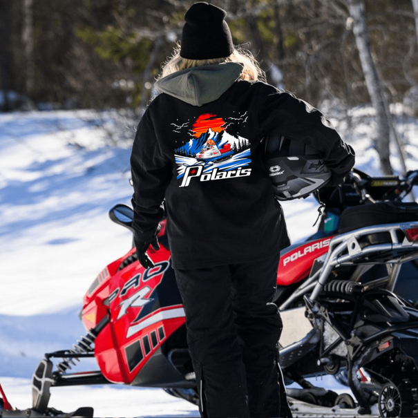 Person wearing a Polaris jacket on a snowmobile in a snowy landscape