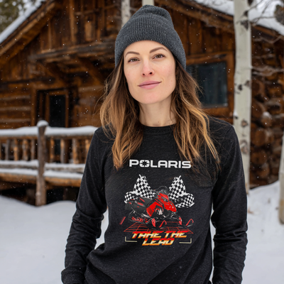 Woman wearing a Polaris shirt in front of a wooden cabin in the snow