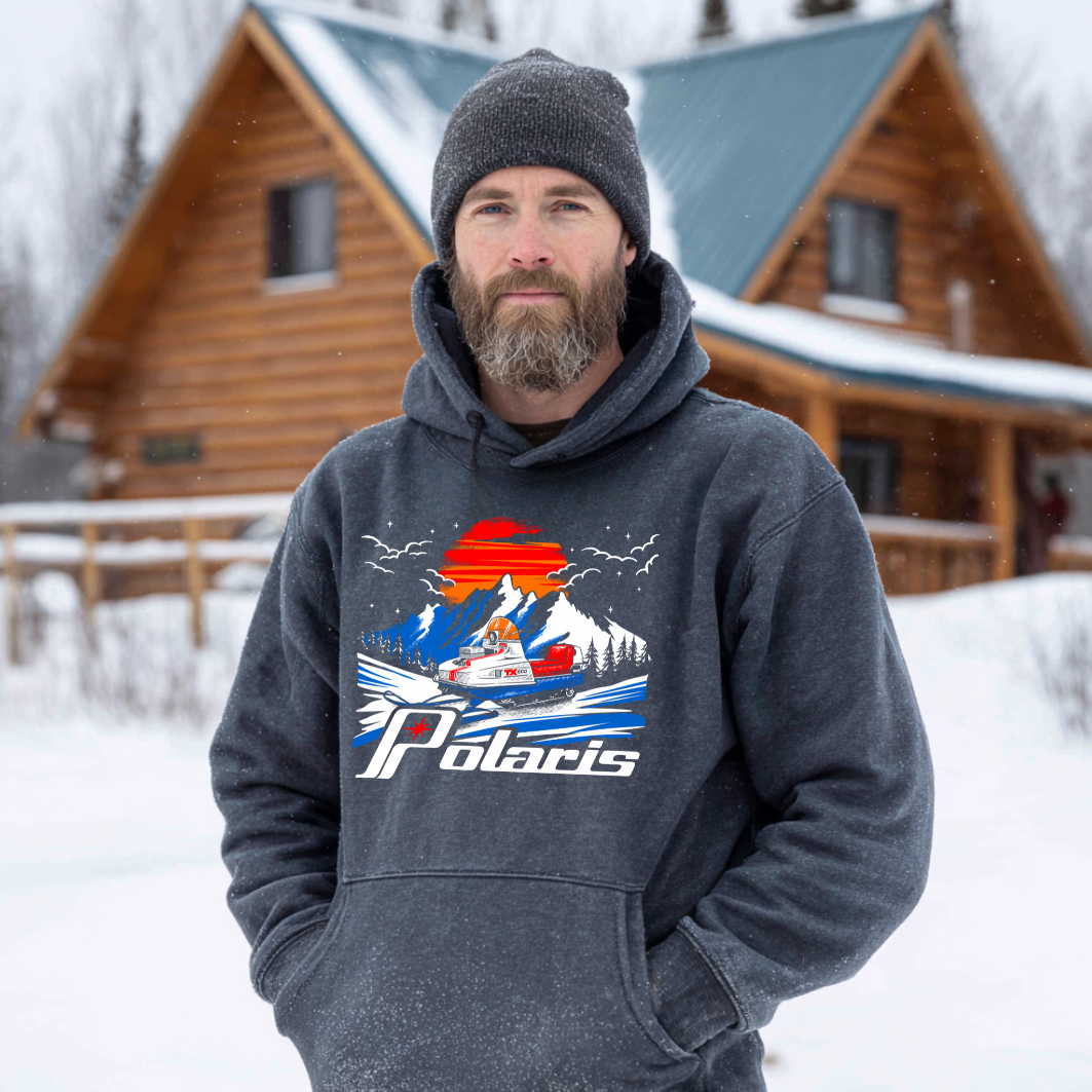 Man wearing a hoodie with a Polaris logo in front of a wooden cabin in the snow.