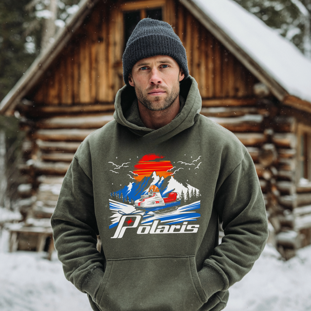 Man wearing a green hoodie with a Polaris graphic in front of a wooden cabin in the snow.