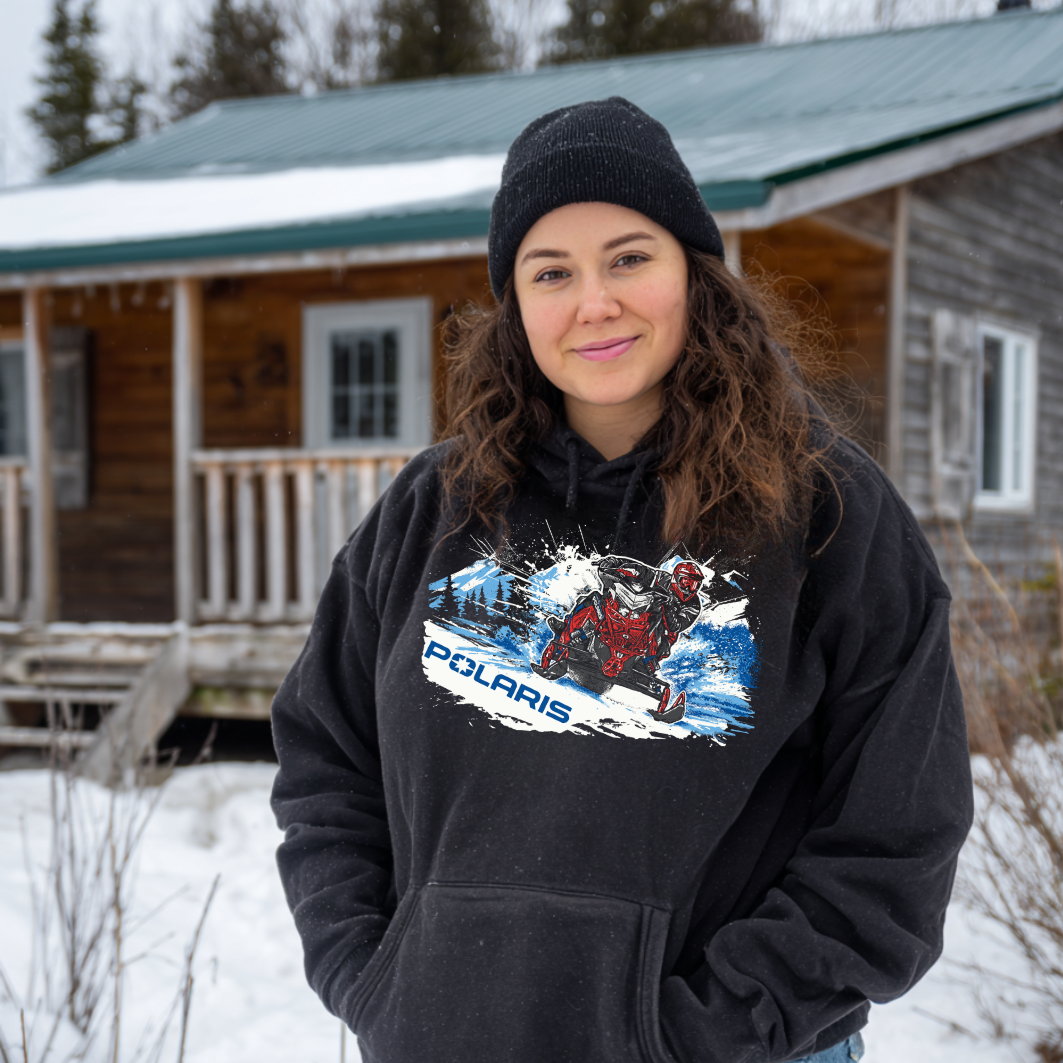 Woman wearing a black hoodie with Polaris graphic in front of a wooden cabin in the snow.