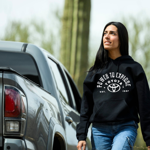 Woman wearing a black hoodie with Toyota logo and text, standing next to a truck outdoors.