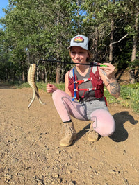 Person holding a snake and a stick in a forested area