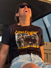 Person wearing a black t-shirt with a Land Cruiser graphic and text, sitting inside a vehicle.