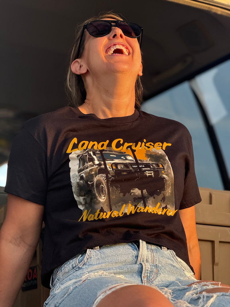 Person wearing a black t-shirt with a Land Cruiser graphic and text, sitting inside a vehicle.