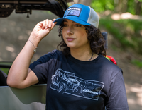 Person wearing a blue cap with Polaris logo and black t-shirt with vehicle graphic, standing next to a vehicle.