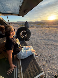 Person sitting on a vehicle in a desert landscape with a sunset.
