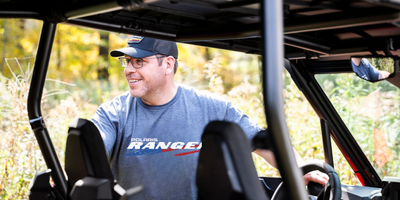 Man wearing a Polaris Ranger shirt inside an off-road vehicle with a blurred natural background