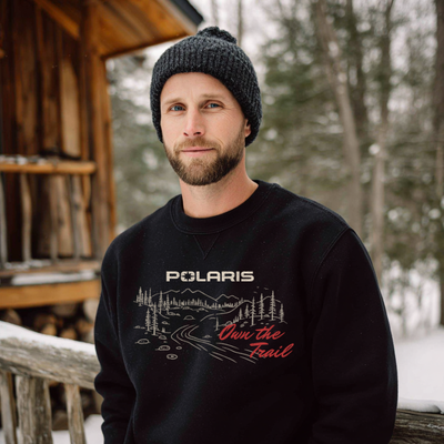 Man wearing a black Polaris sweatshirt with a forest design in a snowy outdoor setting.