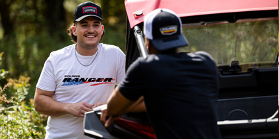 Two men standing next to a Polaris Ranger vehicle in an outdoor setting