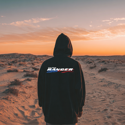 Person wearing a hoodie with 'Polar Ranger' logo in a desert at sunset