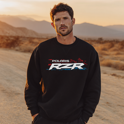 Man wearing a black Polaris RZR sweatshirt in a desert setting with mountains in the background.