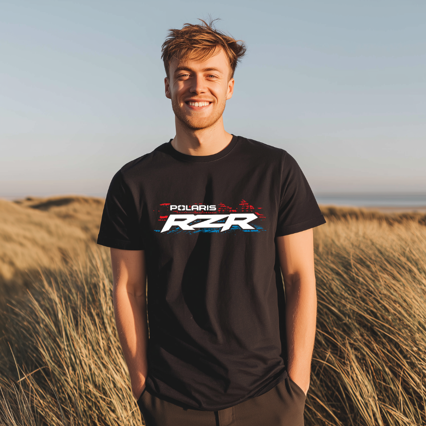 Person wearing a black Polaris RZR t-shirt standing in tall grass with a clear sky.