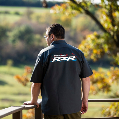 Man wearing a Polaris RZR shirt standing on a wooden deck with a scenic background