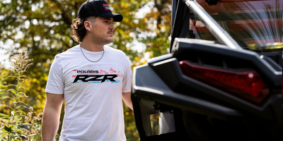 Man wearing a Polaris RZR shirt standing next to a vehicle with a blurred background