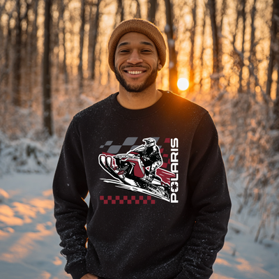Man wearing a black sweatshirt with Polaris graphic in a snowy forest at sunset