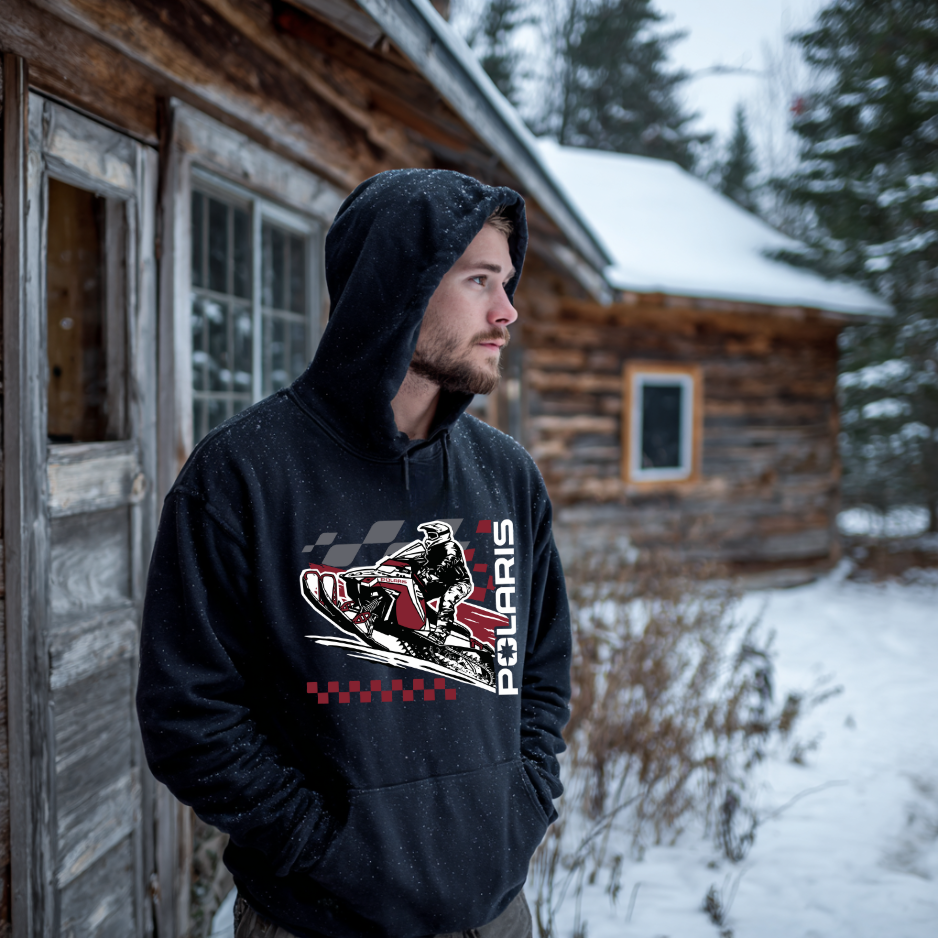Man wearing a black hoodie with a Polaris graphic in front of a wooden cabin in a snowy landscape.