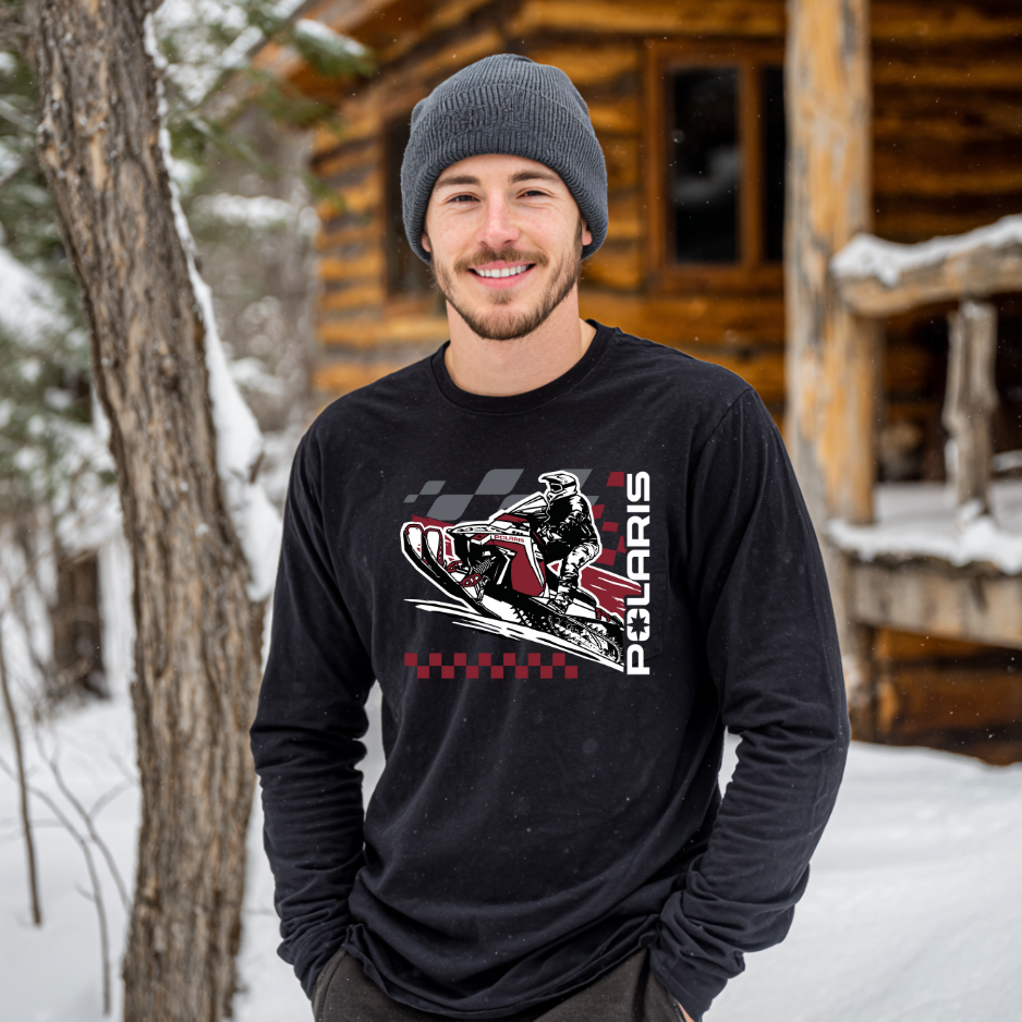 Man wearing a black Polaris-themed shirt standing in front of a wooden cabin in the snow.
