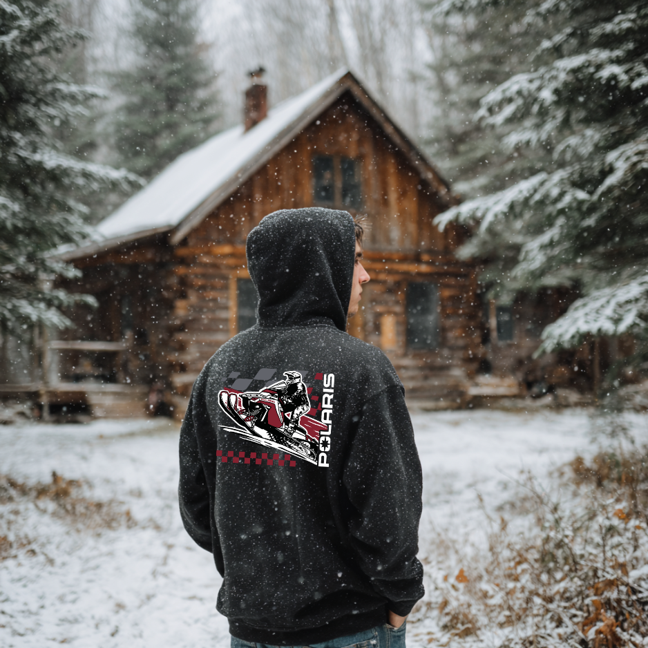 Person wearing a black hoodie with Polaris logo in front of a snow-covered cabin.