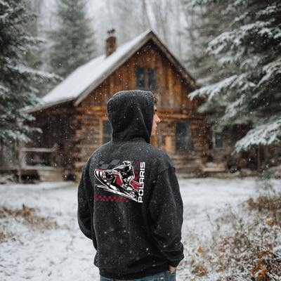 Person wearing a black hoodie with Polaris logo in front of a snow-covered cabin.